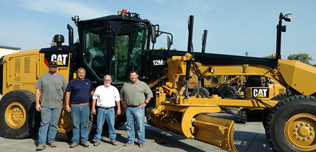 4 men standing in front of bulldozer smiling