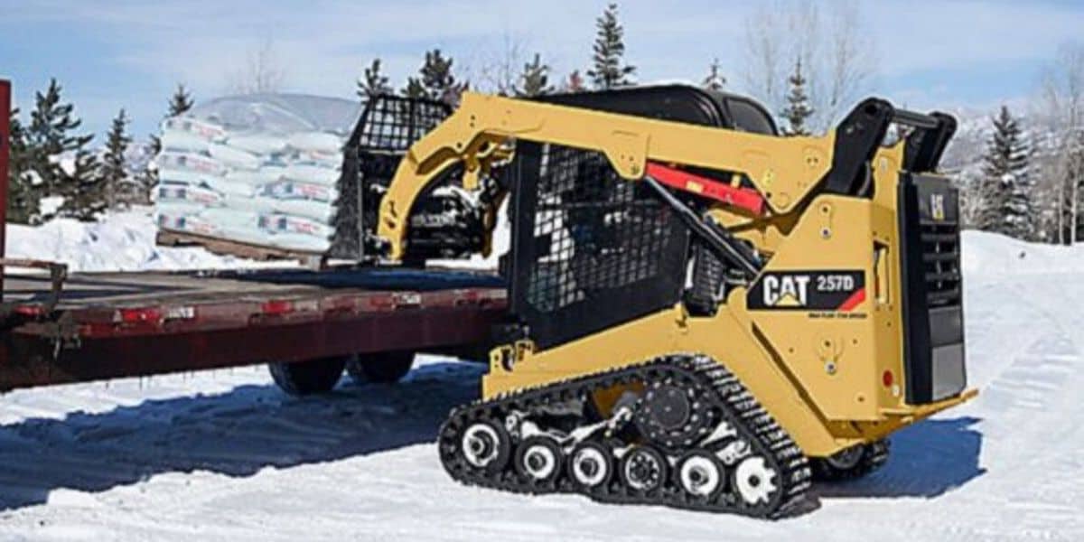 Track loader lifting salt onto truck in snowy field