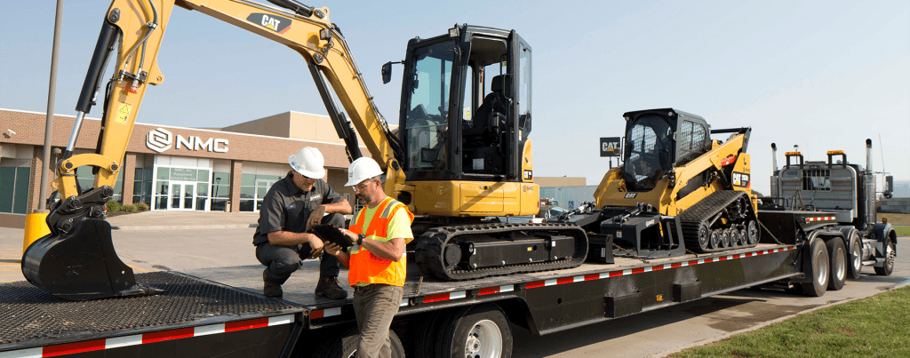 Two men talking in front of a truck carrying Cat heavy equipment