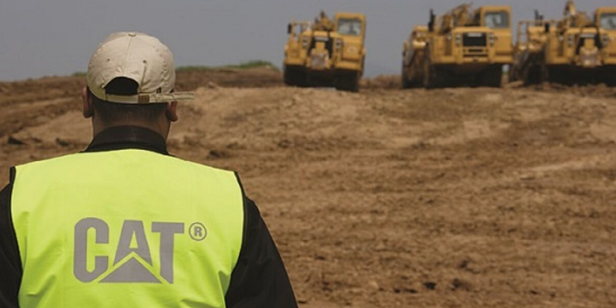 CAT worker standing facing three trucks in a dirt field