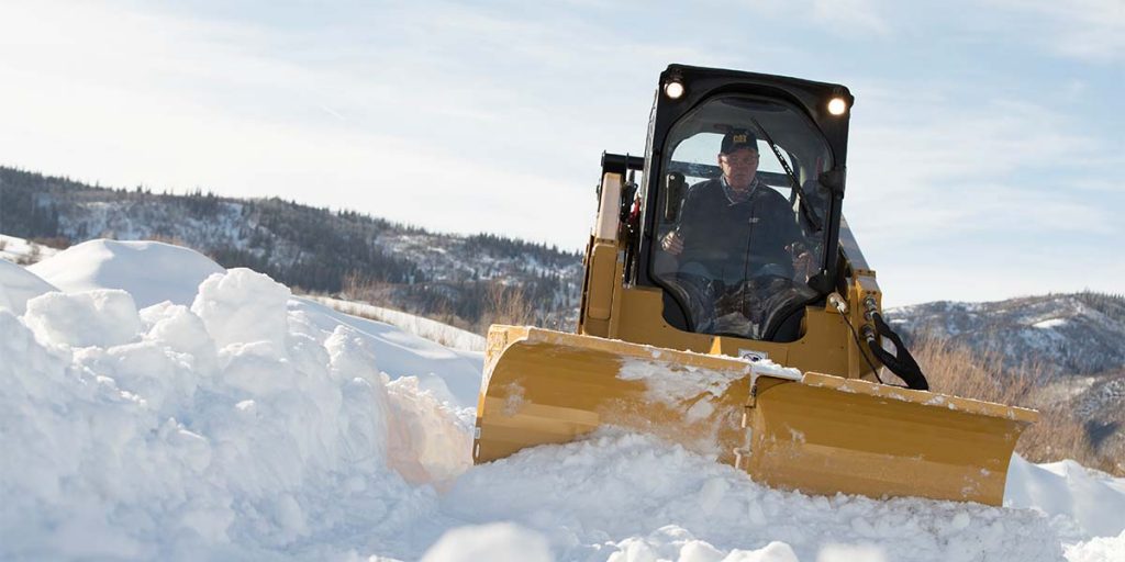 Older man driving Cat tractor in the snow