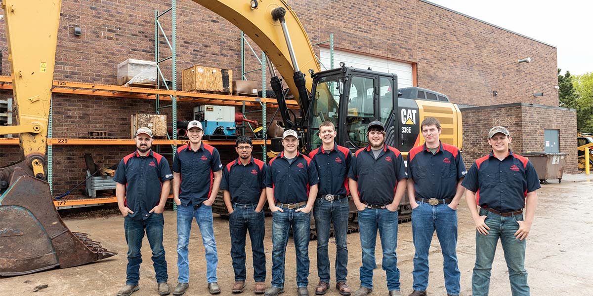 Group central community college partners standing with hands in front pockets in front of excavator