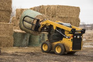 Cat skid steer loader moving large hay bales